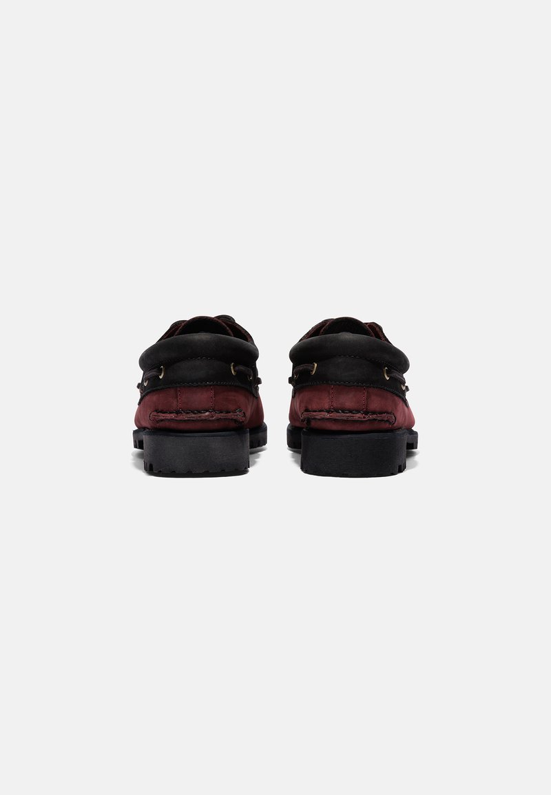 Mocasines rojos y negros con un upper suave, puntera redonda y suela de goma texturizada. Presenta dos acentos de hardware en tono dorado en los laterales.
