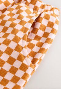 Tissu en coton présentant un motif à carreaux orange et blanc. Les détails incluent une poche visible et une texture douce.
