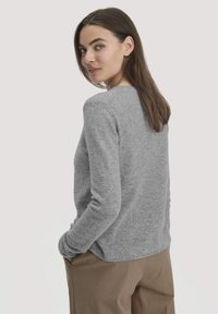 Grauer Pullover mit langen Ärmeln und weicher Textur, rundem Halsausschnitt und subtilen Nahtdetails, kombiniert mit beigen Hosen.
