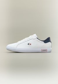 Λευκά sneakers Lacoste χαμηλού τύπου με ναυτικό κολάρο, λευκά κορδόνια, λογότυπο κροκόδειλου στο πλάι και ετικέτα Lacoste στη λευκή καουτσούκ σόλα.