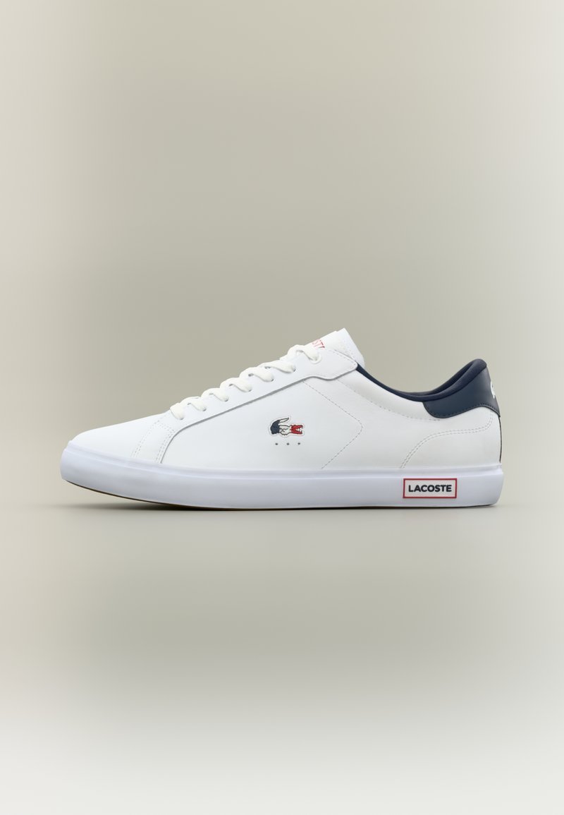 Λευκά sneakers Lacoste χαμηλού τύπου με ναυτικό κολάρο, λευκά κορδόνια, λογότυπο κροκόδειλου στο πλάι και ετικέτα Lacoste στη λευκή καουτσούκ σόλα.