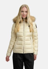 Giubbotto puffo crema con cappuccio staccabile foderato in pelliccia, chiusura con zip e cuciture diagonali. Presenta due tasche laterali e patch con logo sulla manica.