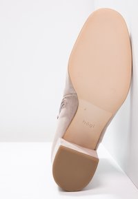 Chaussure habillée en cuir suédé beige avec semelle texturée et talon carr é, la semelle affichant le nom de marque "hōgl", positionnée à la verticale sur un fond blanc.