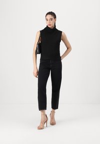 Svart ribbad ärmlös polotröja i kombination med mörka avklippta jeans och nakna högklackade sandaler. En svart väska hänger från axeln.