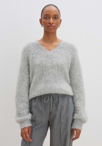 Hellgrauer, flauschiger Pullover mit V-Ausschnitt und langen Ärmeln, kombiniert mit grauen Jogginghosen mit Kordelzug. Strukturierter, weicher Stoff.