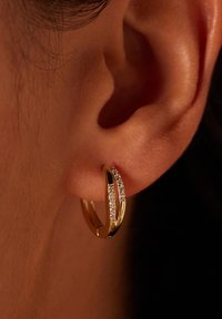 Gouden creolen met een gepolijste afwerking, voorzien van een rij kleine heldere kristallen aan de zijkant, bevestigd aan een close-up van een oor.