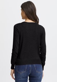 Pulover negru dintr-un material tricotat moale, cu decolteu rotund și mâneci lungi, având o tivă strâmtă. Purtați cu blugi albaștri.