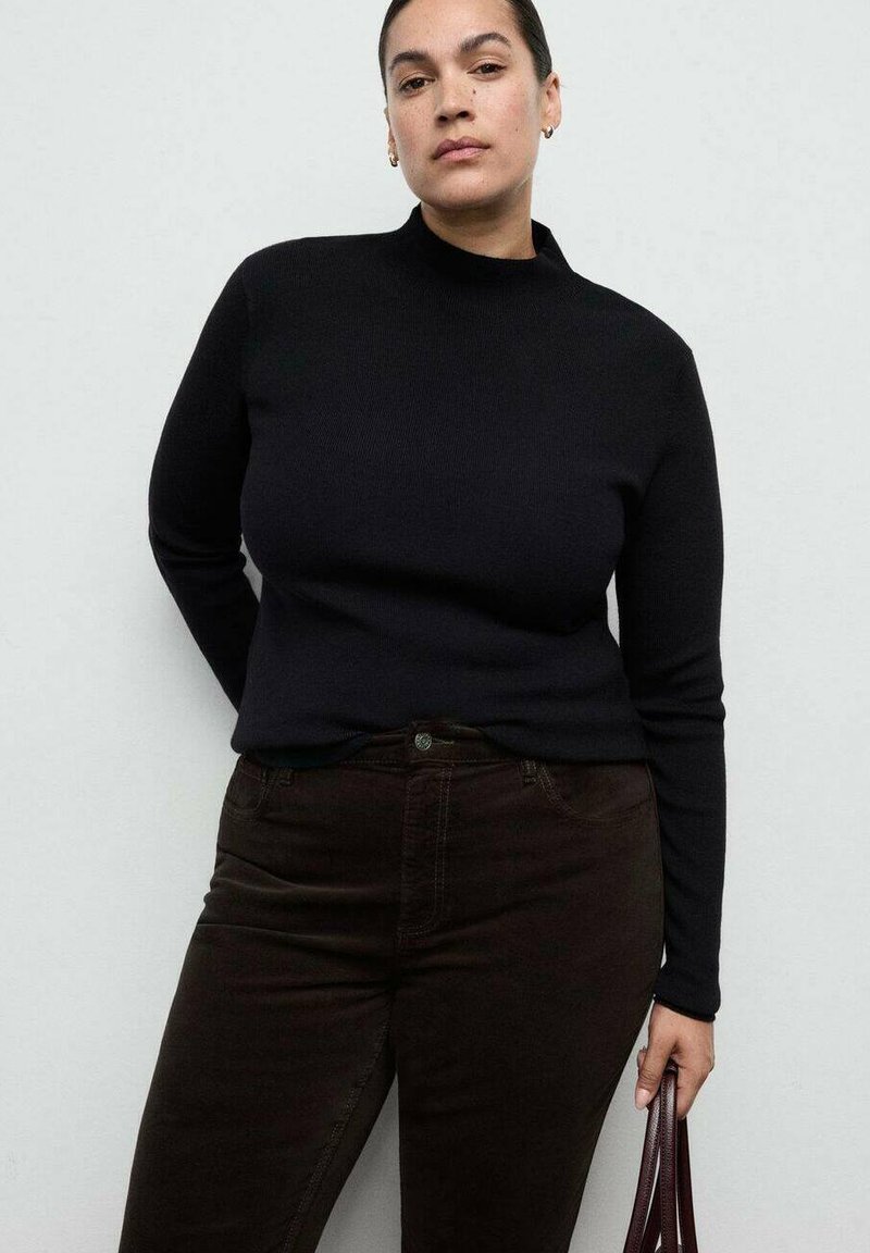 Zwart geribbelde gebreide trui met hoge hals, aansluitende pasvorm, gedragen met donkerbruine jeans, voorzien van subtiele zak- en ceintuurlusdetails.