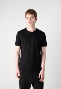 Black crew-neck t-shirt made of smooth cotton fabric, short sleeves, and a relaxed fit. Worn with black pants, minimalistic design.