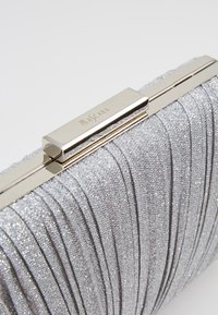 Clutch argent métallique avec une texture plissée, dotée d'un fermoir doré portant un logo. Design compact adapté aux occasions en soirée.
