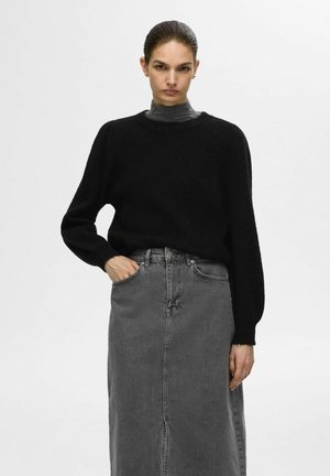 Pull noir en maille lâche avec un col haut, associé à une longue jupe en denim grise avec des poches avant et une couture centrale.