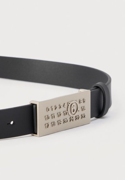 Μαύρη ζώνη με ορθογώνια ασημένια αγκράφα που εμφανίζει αριθμούς από 0 έως 23 σε τέσσερις σειρές και έναν αριθμό 6 μέσα σε κύκλο.