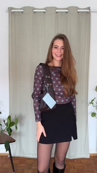 Brown, sleeveless top with blue polka dots, paired with a black wrap skirt. Black knee-high boots and a small blue tag attached to the bag.