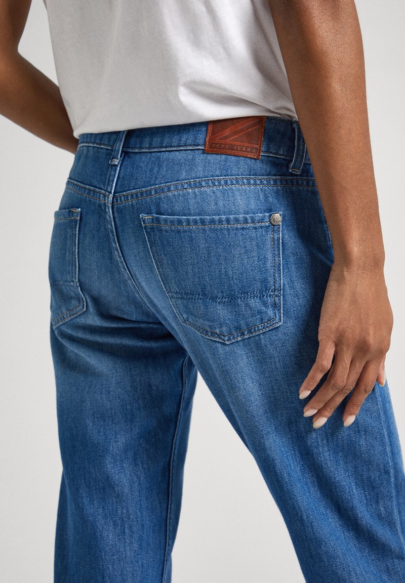 Dunkelblaue Denim-Jeans mit leicht schmaler zulaufender Beinform, mit Gesäßtaschen, einem braunen Leder-Patch am Bund und dezenten Steppdetails.