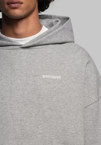Felpa grigia con cappuccio realizzata in tessuto morbido, con il logo bianco "WRSTBHVR". Il design ha una vestibilità comoda con un cappuccio ampio.