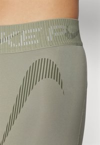 Olivegrønne leggings med en ribbet talje og et struktureret mønster af mørke striber. Glat materiale med et tætsiddende design.