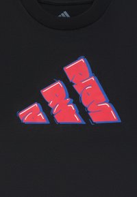 Melnā T-kreklā ir liels stilizēts sarkans un zils grafiskais logo. Materiāls ir gluds, ar apaļu kakla dizainu.