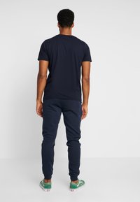 Navyblauwe katoenen T-shirt gecombineerd met navy joggingsbroek en groene sneakers, met een eenvoudig ontwerp en een relaxed pasvorm.