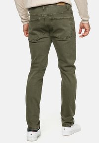 Pantalones de mezclilla verde oliva con corte ajustado, dos bolsillos traseros y cintura a media altura. Llevados con zapatillas blancas y una blusa beige.