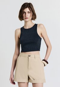 Débardeur court navy à texture côtelée et bretelles larges, associé à un short taille haute beige avec ourlet roulé et fermeture à bouton sur le devant.