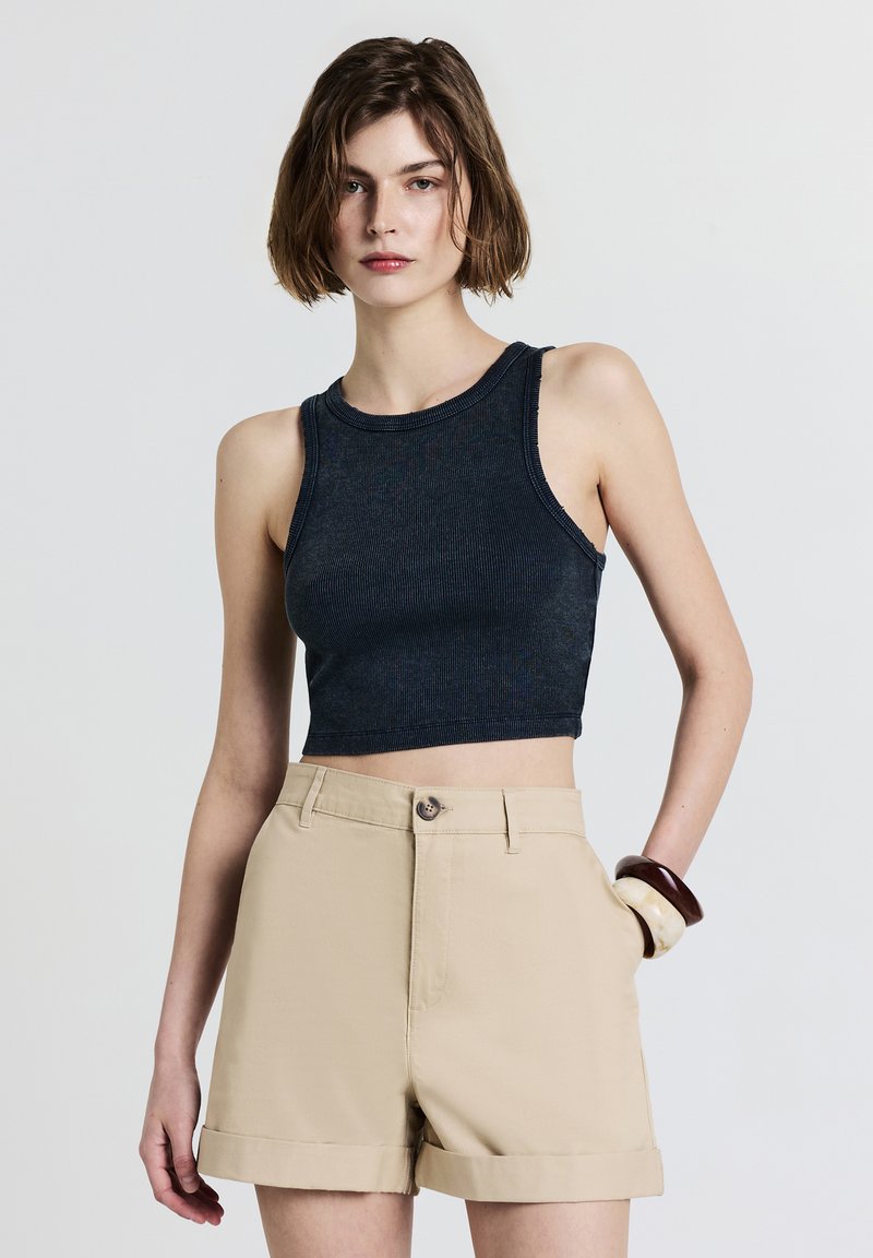 Débardeur court navy à texture côtelée et bretelles larges, associé à un short taille haute beige avec ourlet roulé et fermeture à bouton sur le devant.