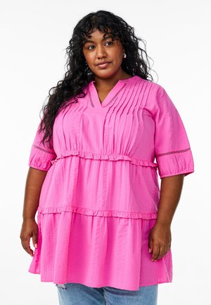 Roze getierde tuniek van textuurstof, met een v-hals, korte mouwen en rimpelaccenten. Casual pasvorm, gecombineerd met lichte jeans.