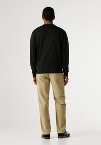 Sweatshirt preta de gola redonda com punhos canelados, combinada com calças de corduroy bege. Pés em sapatilhas pretas com solas castanhas. Design simples e moderno.