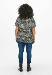 Maglietta a maniche corte con stampa leopardata, scollatura tonda e dettaglio a occhiello, abbinata a jeans blu attillati e stivaletti neri.