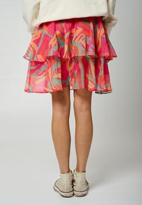 Jupe en couches de couleur rose avec un motif abstrait coloré, agrémenté de accents teal clair, orange et jaune. Fabriquée à partir d'un tissu léger et transparent.