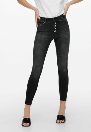 Zwarte skinny jeans met een hoge taille en een vijf-knopen gulp. Voorzien van een paar voorzakken en een gladde denimtextuur. Gekocht met zwarte slide-sandalen.