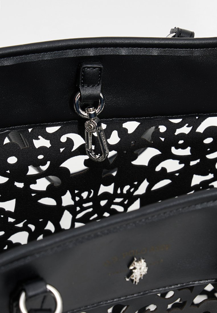 Bolso de mano de cuero negro con un intrincado diseño cortado. Presenta herrajes plateados y un cierre decorativo. El interior tiene una textura suave.