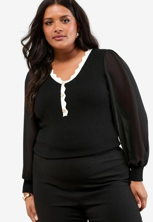 Black ribbed top with white scalloped neckline and button detail, featuring sheer puff sleeves. Paired with black pants for a cohesive look.