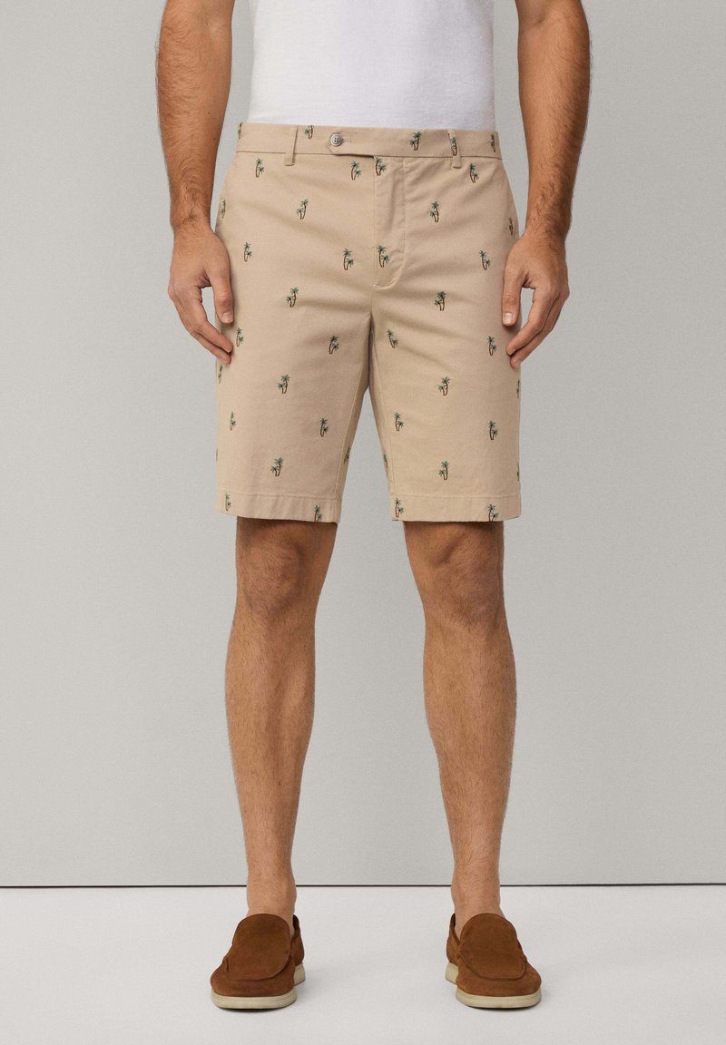 Knee-length beige shorts made from cotton, featuring small green palm tree prints, a flat front, and standard pockets.