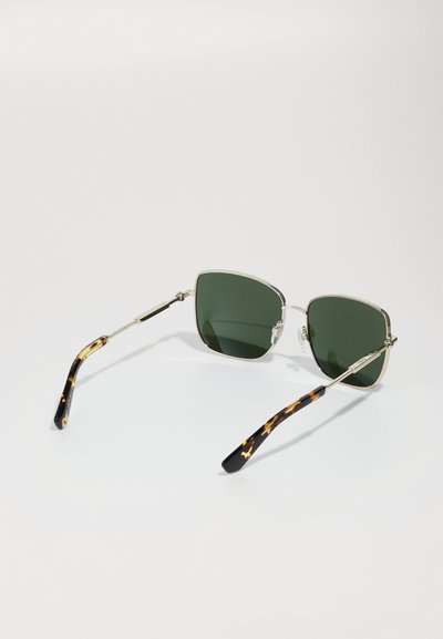 Ochelari de soare cu lentile verzi, ramă din metal argintiu și brațe cu model țestoasă. Formă pătrată cu tampoane nazale transparente și detalii metalice.