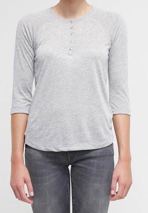 Chemise grise à manches trois-quarts avec un col arrondi et cinq boutons décoratifs, fabriquée dans un tissu doux à texture lisse.
