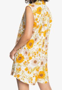 Vestido floral con mangas cortas, con una base blanca y vibrantes girasoles y margaritas amarillas y naranjas. Tejido ligero, corte relajado.