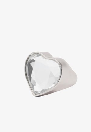 Anillo de plata con una gran piedra preciosa transparente en forma de corazón facetada colocada en la parte superior, mostrado sobre un fondo blanco.