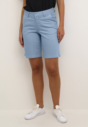 Lyseblå skræddersyede shorts i et blødt stof med flad front, sidelommer og oprevne manchetter, parret med hvide sneakers.