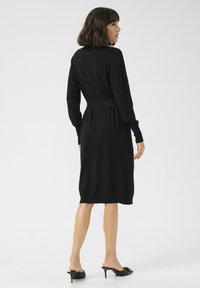 Schwarzes Strickkleid mit langen Ärmeln, taillierter Passform und knielangem Saum. Glatte Textur; minimalistische Gestaltung; Rückansicht gezeigt.