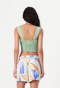 Haut court smocké vert avec des larges bretelles, associé à un short léger à motifs comportant des designs abstraits en bleu, orange et vert.