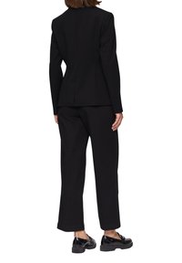 Zwart op maat gemaakt blazer met gestructureerde schouders, getailleerde taille en lange mouwen, gecombineerd met wijde zwarte broek en zwarte schoenen.