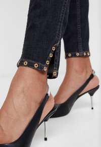 Dark denim jeans with gold eyelet accents at the hem, paired with black slingback heels featuring slender stilettos.