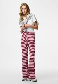 Röda och vita randiga vida byxor med dragsko i midjan, kombinerade med en figurnära vit t-shirt och en grå tröja hängande över axlarna.