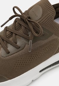 Brune strikkesko med teksturert overdel, geometriske detaljer, båndsnøring og hvit såle. GEox-logo på siden. Kontrasterende matte og glansfulle materialer.