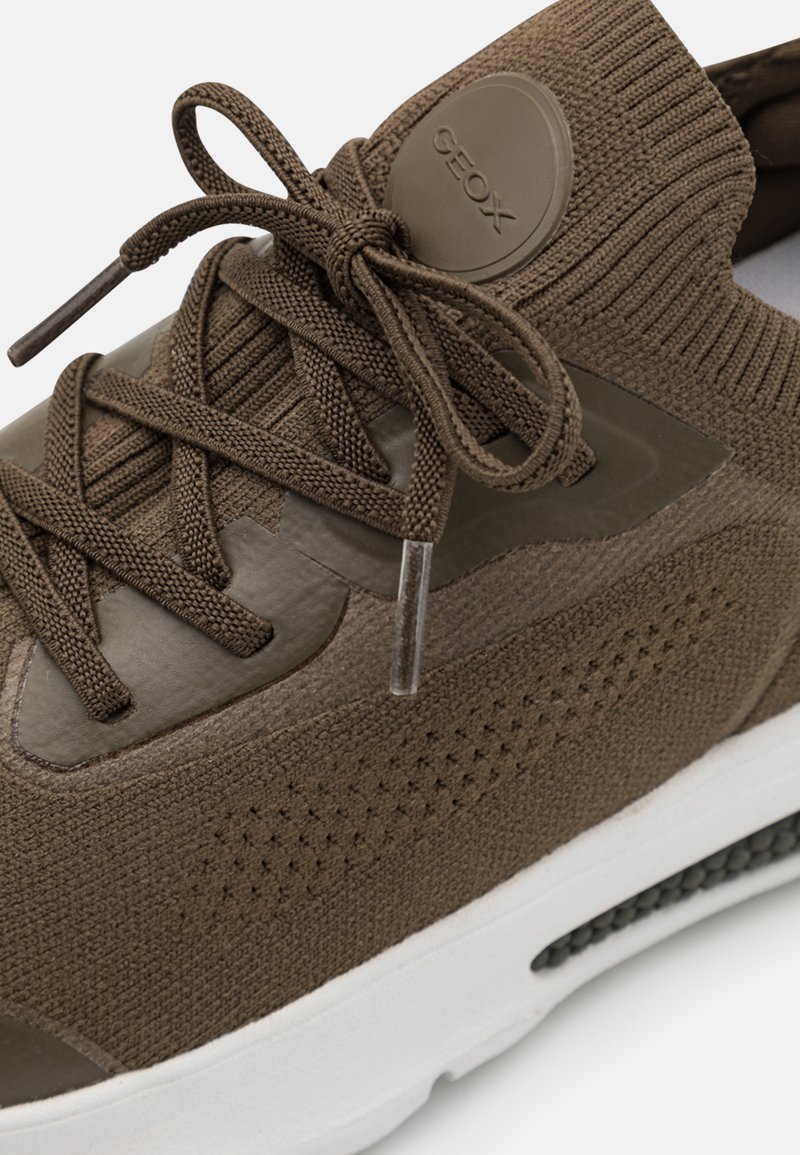 Braune Strick-Sneaker mit strukturiertem Obermaterial, geometrischen Akzenten, Ripsband-Schnürsenkeln und einer weißen Sohle. GEox-Logo an der Seite. Kontrastierende matte und glänzende Materialien.