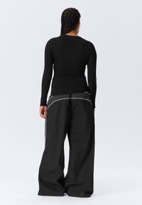 Black long-sleeve fitted top with a smooth texture. High-waisted black wide-leg pants with white stitching and side accents.