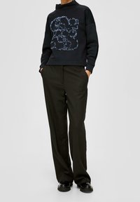 Sudadera negra con cuello alto y un diseño azul estampado, combinada con pantalones negros holgados y zapatos negros de suela gruesa. Textura suave.