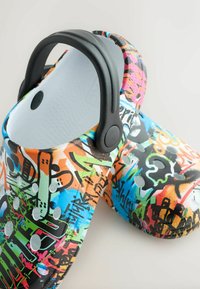 Sabots colorés à enfiler avec un imprimé style graffiti, des trous d'aération et une bride de talon noire réglable.