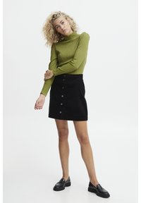 Maglione verde a coste con collo alto e maniche lunghe, abbinato a una gonna A-line in corduroy nera con dettagli di bottoni frontali e una vita.