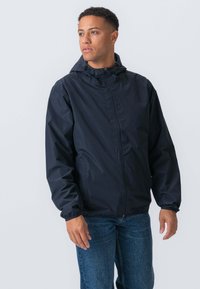 Mørkeblå letvægtsjakke med hætte, elastiske manchetter og frontlynlås. Har en glat tekstur og en afslappet, tætsiddende design.